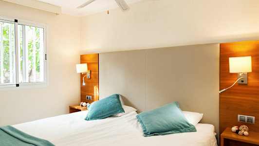 Valoisa makuuhuone, jossa on parivuode, sinisiä tyynyjä ja ikkuna. (Tekoälyn luoma teksti)