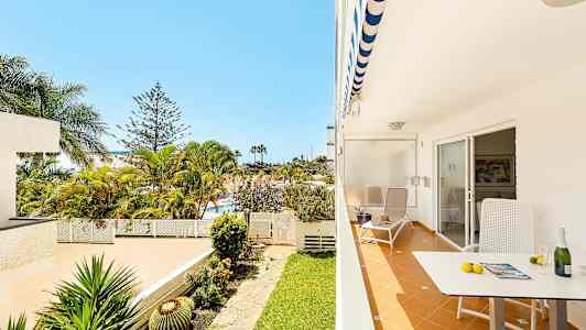 Terassi, jossa tuoli ja pöytä, näkymä puutarhaan palmuineen. (Tekoälyn luoma teksti)