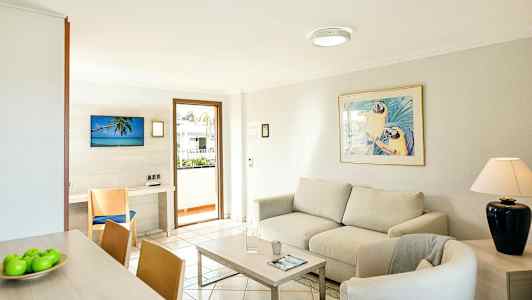 Valoisa olohuone, jossa sohva, nojatuoli, sohvapöytä ja koristeltu taulu sohvan yläpuolella. (Tekoälyn luoma teksti)