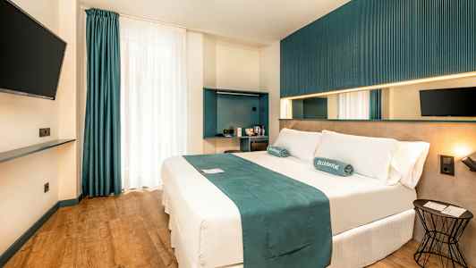 Moderni hotellihuone, jossa on parivuode, seinälle kiinnitetty televisio ja minimalistinen sisustus. (Tekoälyn luoma teksti)