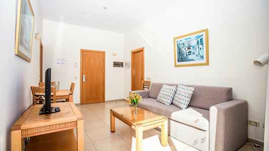 Hotellihuone, jossa on sohva, ruokapöytä ja televisio. (Tekoälyn luoma teksti)