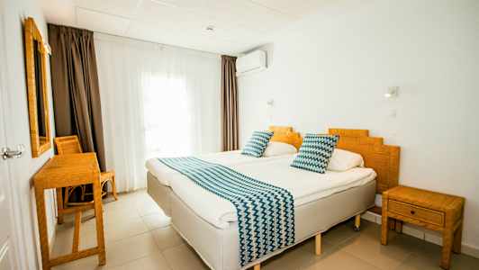 Hotellihuone, jossa kaksi yhden hengen vuodetta, bambukalusteet ja valkoiset seinät. (Tekoälyn luoma teksti)