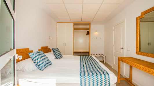 Hotellihuone, jossa on sänky, vuodevaatteet ja peili. (Tekoälyn luoma teksti)