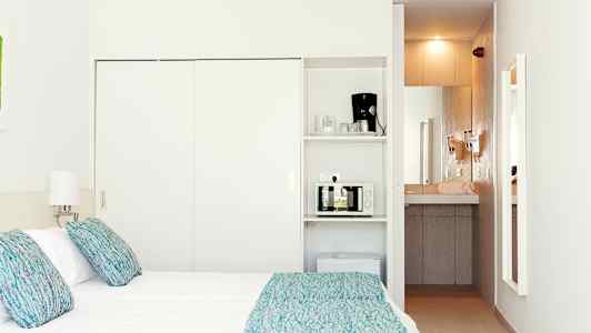 Hotellihuone, jossa on sänky, lamput ja minikeittiö, johon kuuluu mikroaaltouuni ja kahvinkeitin. (Tekoälyn luoma teksti)