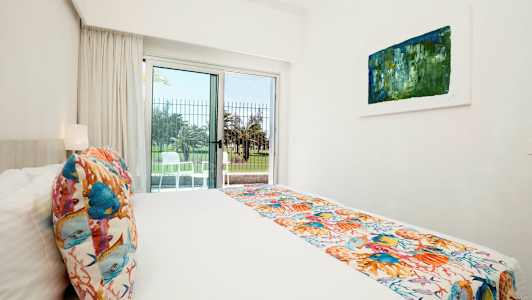 Vaalea hotellihuone, jossa on sänky, värikkäitä koristeita ja avautuminen terassille. (Tekoälyn luoma teksti)
