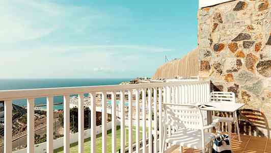 Näköala parvekkeelta, jossa pöytä ja tuolit, sekä näkymä merelle ja ympäristöön. (Tekoälyn luoma teksti)