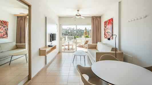 Moderni hotellihuone, jossa kaksi sohvaa, ruokapöytä ja tuoleja sekä parveke näkymällä. (Tekoälyn luoma teksti)