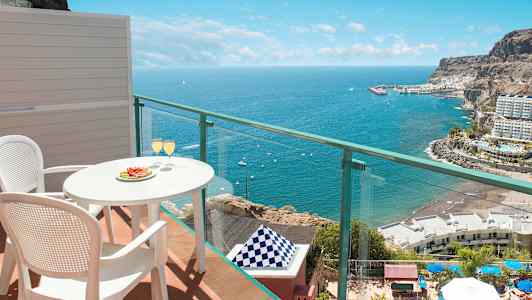 Näkymä parvekkeelta, pöytä ja kaksi tuolia, tarjoillut lasit, meri ja rannikko maisemaan. (Tekoälyn luoma teksti)