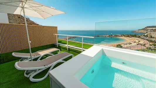 Terassi, jossa aurinkotuoleja, aurinkovarjo ja pieni uima-allas, näkymä rannalle ja merelle. (Tekoälyn luoma teksti)