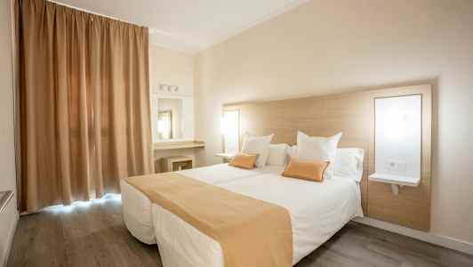 Hotellihuone, jossa on kaksi erillistä vuodetta ja beige-valkoinen värimaailma. (Tekoälyn luoma teksti)