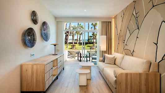 Modernisti sisustettu olohuone, jossa on puuyksityiskohtia ja beige sohva, näkymä vihreään puutarhaan lasiovien läpi. (Tekoälyn luoma teksti)