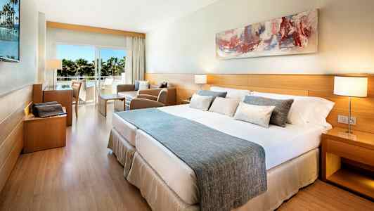 Hotellihuone, jossa on parisänky, oleskelualue ja parveke näkymällä. (Tekoälyn luoma teksti)