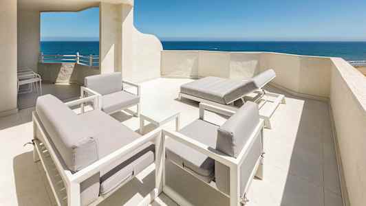 Kattohuoneiston terassi, jossa valkoiseksi maalattua sisustusta ja näkymä merelle. (Tekoälyn luoma teksti)