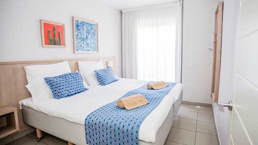 Kuva hotellihuoneesta, jossa on parisänky, sinisiä yksityiskohtia ja taideteoksia seinällä. (Tekoälyn luoma teksti)