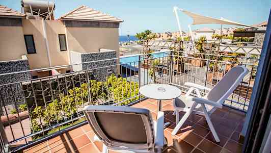 Parveke, jossa kaksi tuolia ja pöytä, näkymä rakennuksille ja uima-altaalle. (Tekoälyn luoma teksti)