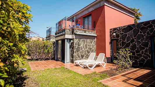 Loma-asunto, jossa terassi ja aurinkotuolit, ympäröitynä puilla ja vihreällä. (Tekoälyn luoma teksti)