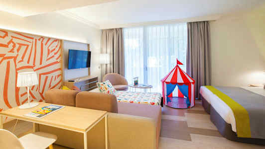 Hotellihuone, jossa värikäs sirkusteltta-lelu sängyn vieressä. (Tekoälyn luoma teksti)