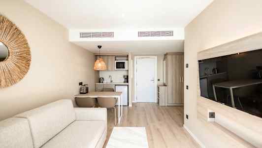 Moderni hotellihuone, jossa mukava sohva, keittiötila, ruokapöytä ja taulutelevisio. (Tekoälyn luoma teksti)