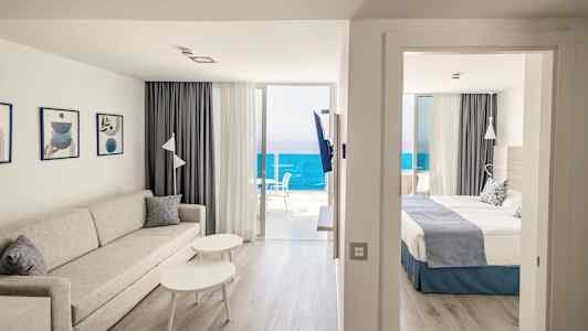 Olohuone, jossa sohva ja pöytä makuuhuoneen vieressä. Merinäköala parvekkeelta. (Tekoälyn luoma teksti)