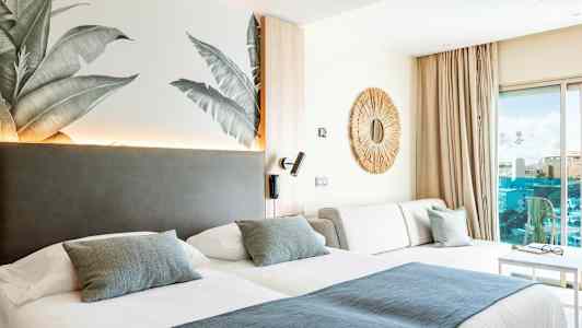 Hotellihuone, jossa on kaksi sänkyä, sohva ja koristeellinen peili seinällä. (Tekoälyn luoma teksti)