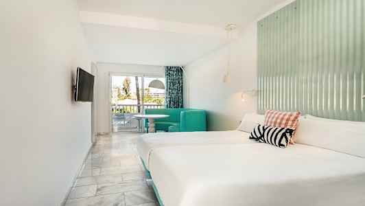 Hotellihuone, jossa parivuode, istuinryhmä ja parvekkeen uloskäynti. (Tekoälyn luoma teksti)