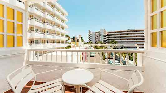 Parveke, jossa kaksi tuolia ja pöytä, näkymä läheisiin rakennuksiin. (Tekoälyn luoma teksti)