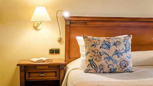 Sänky puupinnalla, koristetyyny ja kirja yöpöydällä. (Tekoälyn luoma teksti)