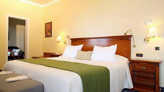 Hotellihuone, jossa on leveä sänky, vihreä päiväpeitto ja puukalusteet. (Tekoälyn luoma teksti)