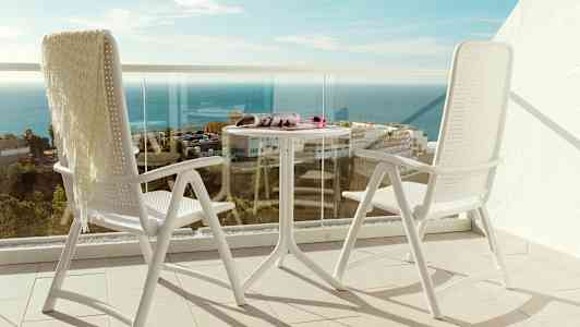 Kaksi valkoista tuolia ja pöytä parvekkeella, josta näkyy merelle. (Tekoälyn luoma teksti)