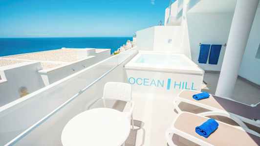 Terassi, jolta on näkymä merelle. Aurinkotuoleja, pöytä ja pieni uima-allas. (Tekoälyn luoma teksti)