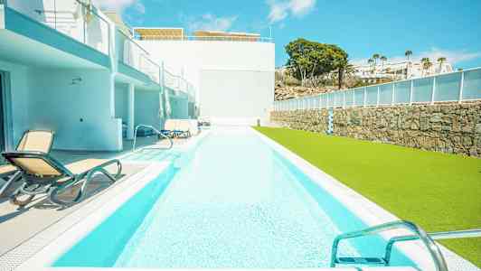 Pitkä uima-allas, jonka vieressä on aurinkotuoleja ja vihreä nurmikko. (Tekoälyn luoma teksti)