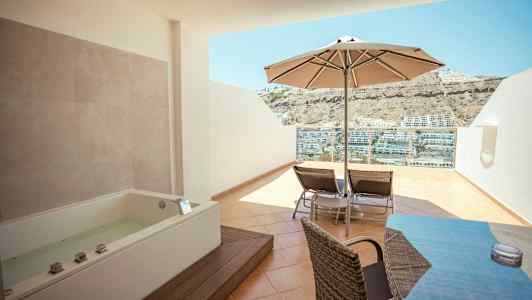 Terassi porealtaalla, aurinkovarjo, aurinkotuoleja ja näkymä taloille rinteessä. (Tekoälyn luoma teksti)