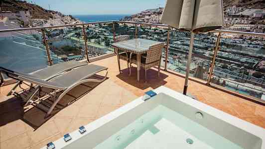 Terassi, jolla on aurinkotuoleja, pöytä ja näköala merelle ja kaupunkiin. (Tekoälyn luoma teksti)