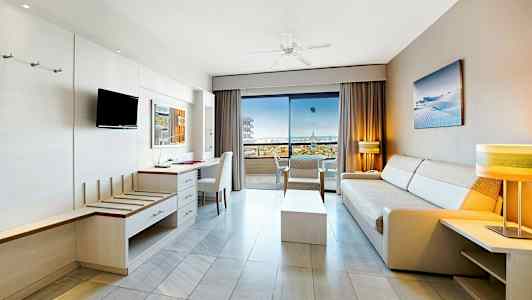 Vaalea hotellihuone, jossa sohvia ja huonekaluja, avoinna parvekkeelle, josta merinäköala. (Tekoälyn luoma teksti)