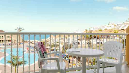 Näkymä parvekkeelta, jossa on valkoiset kalusteet, kohti uima-allasta ja merinäköalaa. (Tekoälyn luoma teksti)