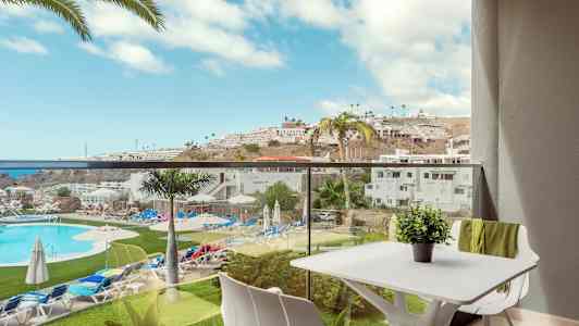 Näkymä parvekkeelta, josta avautuu näkymä uima-altaalle ja ympäröivälle lomakylälle aurinkoisena päivänä. (Tekoälyn luoma teksti)