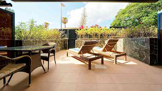 Terassi, jossa on aurinkotuoleja, pöytä ja tuoleja, ympärillä kasveja. (Tekoälyn luoma teksti)