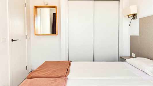 Hotellihuone, jossa valkoiset sisusteet, parivuode valkoisilla lakanoilla ja ruskeilla peitteillä sekä peili seinällä. (Tekoälyn luoma teksti)