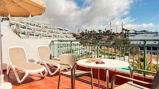 Terassi, jossa on kaksi aurinkotuolia, pöytä ja tuoleja sekä näkymä allasalueelle ja palmuihin. (Tekoälyn luoma teksti)