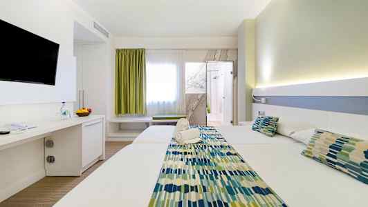 Hotellihuone, jossa kaksi sänkyä, tv seinällä ja oviaukko kylpyhuoneeseen. Huoneessa on vaalea sisustus. (Tekoälyn luoma teksti)