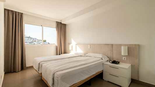 Hotellihuone, jossa on parivuode ja ikkuna, josta näkyy valkoinen rakennus. (Tekoälyn luoma teksti)