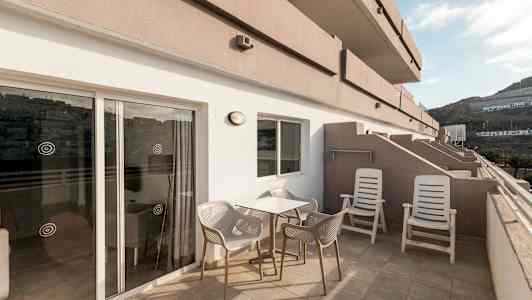 Terassi, jossa on pöytä, tuoleja ja aurinkotuoleja, sekä näkymä ympäröiviin rakennuksiin ja vuorille. (Tekoälyn luoma teksti)