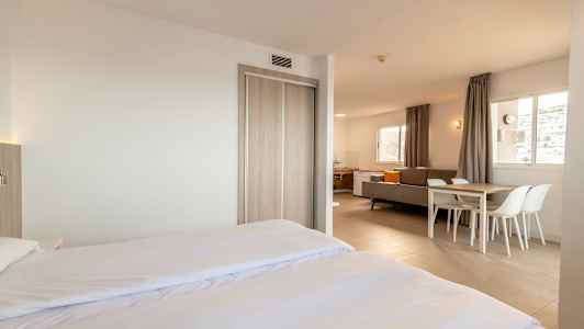 Moderni ja valoisa hotellihuone, jossa parivuode, oleskelualue ja ruokapöytä. (Tekoälyn luoma teksti)