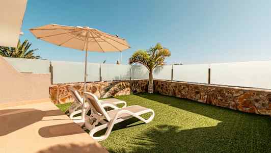 Terassi, jossa on kaksi aurinkotuolia, aurinkovarjo ja tekonurmikko. (Tekoälyn luoma teksti)