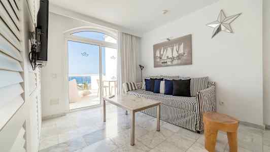 Mustavalkoinen sisustus, jossa sohva ja pöytä huoneessa, jossa on näkymä lasiovien kautta merelle. (Tekoälyn luoma teksti)