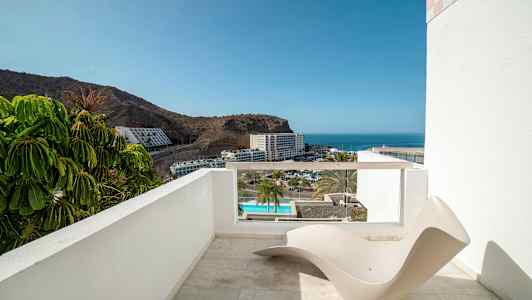 Terassi, jolta on näkymä merelle ja hotellialueelle, etualalla minimalistinen aurinkotuoli. (Tekoälyn luoma teksti)