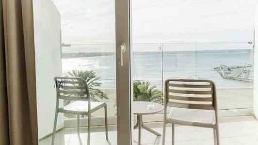 Näkymä parvekkeelta, jossa on kaksi tuolia ja pöytä, rannalle ja merelle. (Tekoälyn luoma teksti)