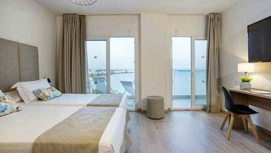 Hotellihuone, jossa on kaksi yhden hengen vuodetta, kirjoituspöytä ja merinäköala lasiovien läpi. (Tekoälyn luoma teksti)