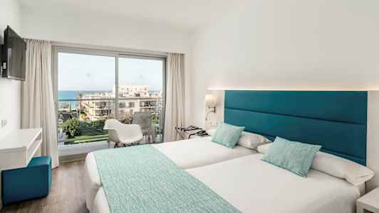 Vaalea hotellihuone, jossa kaksi yhden hengen vuodetta, suuret ikkunat ja näkymä merelle. (Tekoälyn luoma teksti)