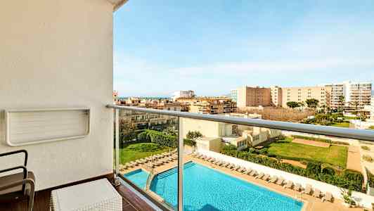 Parveke, jolta näkymä uima-altaalle ja ympäröiviin rakennuksiin. Altaan ympärillä on aurinkotuoleja. (Tekoälyn luoma teksti)